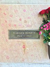 Photo of Monroe's crypt, taken in 2015. "Marilyn Monroe, 1926–1962" is written on a plaque. The crypt is covered in lipstick prints left by visitors and pink and red roses are placed in a vase attached to it.