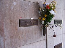 Photo of Monroe's crypt, taken in 2005. "Marilyn Monroe, 1926–1962" is written on a plaque. The crypt has some lipstick prints left by visitors and flowers are placed in a vase attached to it.