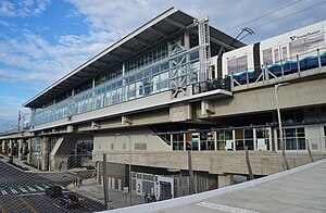 An elevated train station with glass and concrete walls, seen from a bridge jutting out from the middle of the structure.