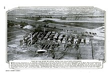 Photographie aérienne en noir et blanc du site industriel, montrant un cratère résultant de l'explosion. Une légende en anglais détaille les conséquences de la catastrophe.
