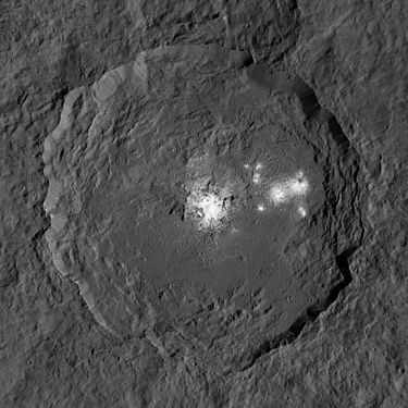 Cràter Occator (92 km) fotografiat per la sonda espacial Dawn a 385 km de distància. Es poden veure unes taques brillants que reben el nom de Cerealia Facula (centre) i Vinalia Faculae (dreta), 2015[4]