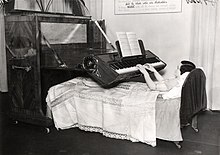 Photographie en noir et blanc d’une femme jouant du piano depuis son lit.