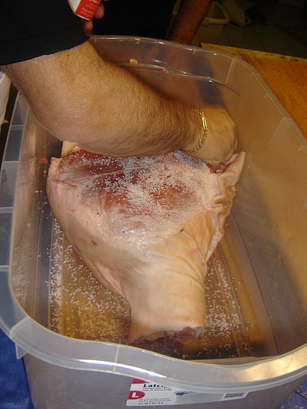 Sea salt being added to raw pork leg as part of a dry cure process