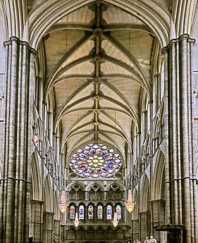 The inside of Westminster Abbey north transept, with a high vaulted ceiling and a rose window at the end.