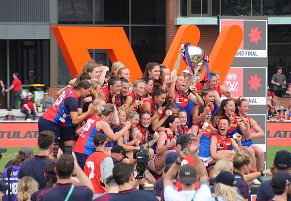 Melbourne players celebrating with their premiership medallions and the 2022 (S7) premiership trophy