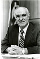 Portrait of a smiling Dr. Ernest Ambler in dark suit and striped tie