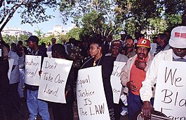 Black farmers protest at Lafayette Park across from the White House in Washington, D.C. on September 22, 1997. Protesters are holding-up signs labeled with phrases. "Don't take our land", "Equal Justice is the Law", and more. But they are cute off.