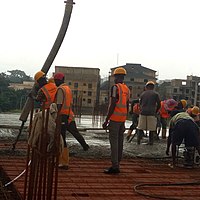 Photo von mehreren Bauarbeitern, teilweise in orange-roten Warnwesten gekleidet, beim Betonieren einer Gebäudedecke.