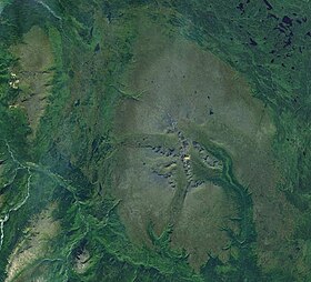 Eine Draufsicht auf bewachsenes Gelände mit zwei großen, felsigen Bergen in der Nähe des Kamms einer Bergkette im Südwesten.