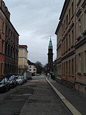 Gerade Straßenabschnitt ohne Fahrbahnmarkierung, links: Autos, rechts Gehweg, rechts hinten: Turm der Lutherkirche