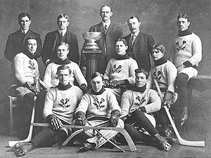 Pierwsza drużyna hokeja na lodzie pozuje do zdjęcia z małym pucharem mistrzowskim pośrodku.