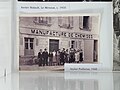 Photographie en noir et blanc. Devant un bâtiment à façade en pierre avec plusieurs fenêtres aux volets ouverts, au fronton duquel on lit « Manufacture de chemises », une quinzaine de personnes, dont une dizaine de femmes et 5-6 hommes, posent debout face à l'objectif. Tous et toutes ont des tenues sobres. Les femmes sont en robe longue ou pull et jupe longue et portent les cheveux courts ou en chignon. Les hommes sont en salopette et veste, ou en complet. Un homme sur la gauche porte un costume élégant avecu un chapeau sombre. Vers la droite, un autre porte un béret noir.