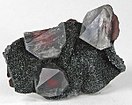 Three gemmy quartz crystals containing bright rust-red inclusions of hematite, on a field of sparkly black specular hematite