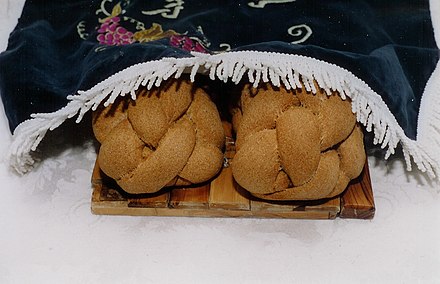 Two homemade challot covered by a traditional embroidered challah cover