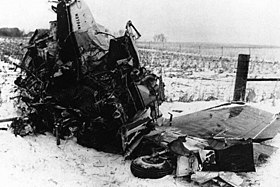 A tangled mass of metal with a wing and landing gear wheel barely recognizable, on a snowy field