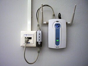 In this configuration, an Ethernet connection includes Power over Ethernet (PoE) (gray cable looping below), and a PoE splitter provides a separate data cable (gray, looping above) and power cable (black, also looping above) for a wireless access point (WAP). The splitter is the silver and black box in the middle between the wiring junction box (left) and the access point (right). The PoE connection eliminates the need for a nearby power outlet. In another common configuration, the access point or other connected device includes internal PoE splitting and the external splitter is not necessary. ZyXEL ZyAIR G-1000 and D-Link DWL-P50 20060829 2.jpg
