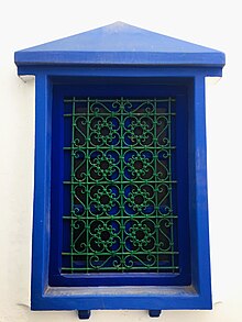 A window displaying a wrought iron window grill in Asila. The knots are tied with bent metal in the traditional way, rather than soldered. nfdh@ mGrby@ fy mdyn@ 'Syl@.jpg