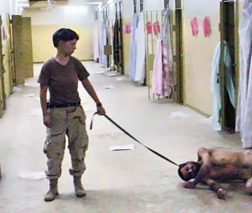 Lynndie England holding a leash attached to a naked male prisoner, known to the guards as "Gus"