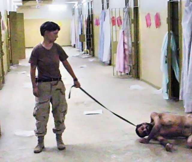 Lynndie England holding a leash attached to a naked male prisoner, known to the guards as "Gus"