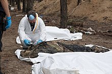 Muž v ochrannej kombinéze skúma exhumované telo