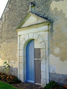 Porte d'entrée en arc plein cintre surmontée d'une croix en pierre de la chapelle Sainte-Camille de Chevigny.