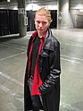 Giovane Cosplayer che indossa i panni di Spike comprendenti la classica giacca di pelle di Nikki Wood, la camicia rossa e i jeans scuri.