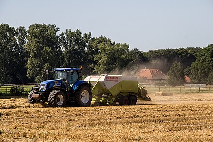 A tractor towing a baler makes hay bales in a field in Germany.