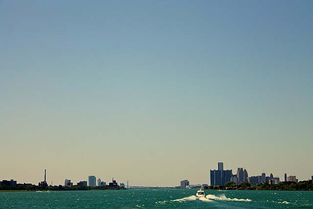 Detroit skyline to the right and Windsor to the left of the Detroit River, with the Ambassador Bridge partially visible in the background