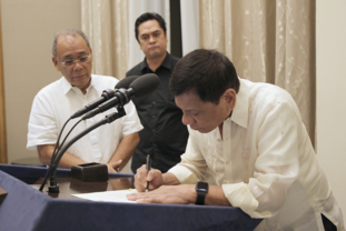 Former spokesperson Ernesto Abella and PCOO secretary Martin Andanar while President Rodrigo Duterte signs Executive Order No. 2, operationalizing the freedom of information in the executive branch FOI Signing.png