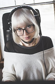 Une femme aux cheveux blancs, avec un casque et des lunettes regarde la caméra.