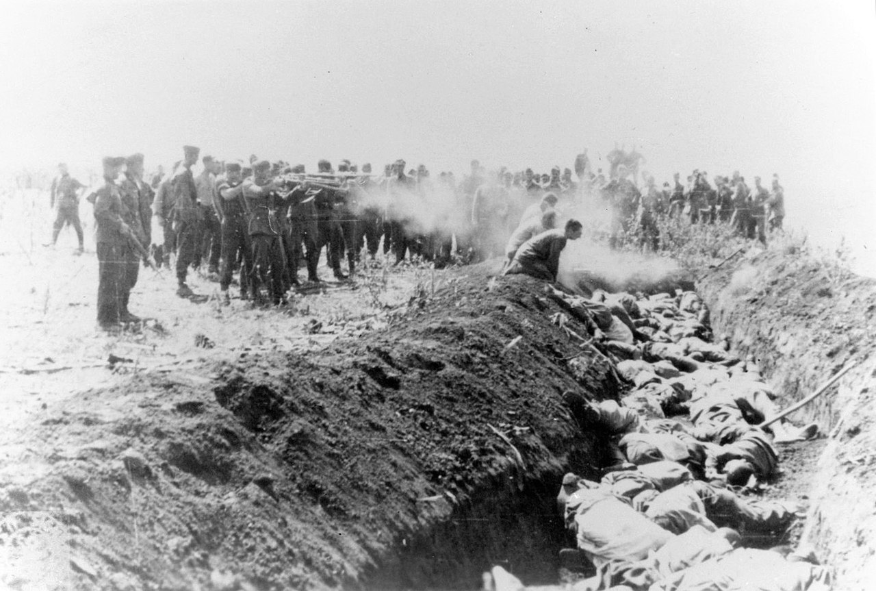 Men with an unidentified unit execute a group of Soviet civilians kneeling by the side of a mass grave.jpg