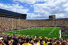 Přeplněný stadion se žlutým nápisem „Michigan“ napsaný na zeleném poli