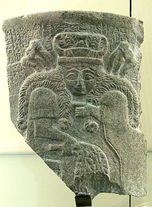 Fragmento de un jarrón de piedra oscura que representa a una mujer con largos cabellos trenzados.
