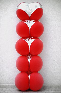 contre un mur, une sculpture de cinq gros ballons rouges empilés, chacun enserré dans une culotte argentée qui lui donne des airs de fesses.