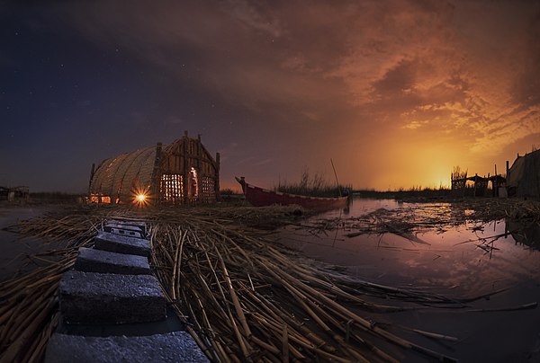 Mesopotamian Marshes at night, southern Iraq; reed house (Mudhif) and narrow canoe (Mashoof) in the water. Mudhif structures have been one of the trad