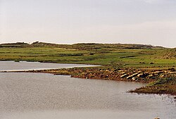 Ein See mit einem felsigen und grünen Küstenvorland