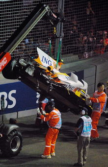 Mobil Renault R28 berwarna putih, kuning dan oranye dalam keadaan rusak yang sedang diangkut oleh mobil derek sesaat setelah kecelakaan yang dialami oleh Nelson Piquet Junior terjadi di Marina Bay Street Circuit di Singapura tahun 2008.
