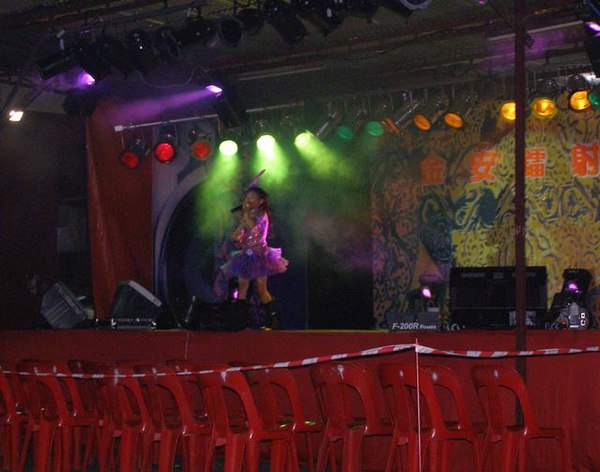 A young girl performing during Ghost Festival in Kuala Lumpur, Malaysia. The red seats in front are reserved for ghosts.