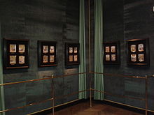 Cinq vitrines contenant les miniatures accrochées sur un mur de velours vert derrière une rambarde.