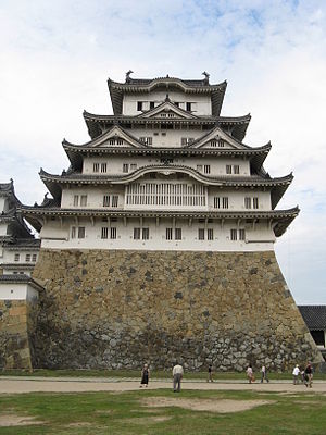A large castle tower with white walls and dark roofs on a platform of unhewn stones.