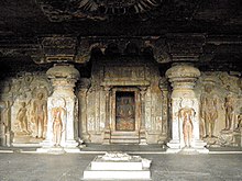 Indra Sabha is the largest of the Jain series and dates from the 9th century, Rashtrakuta patronage. A simple gateway leads to a courtyard in which there is a monolithic shrine with a pyramidal roof. The double-storey temple is excavated in the rear of the courtyard. The interior of the cave has a columned mandapa or hall with niches on the three sides and the sanctuary in the middle of the back wall. Carved figures of the Jain Tirthankharas decorate the walls. Inner sanctum with Mahavira statue, Ellora Cave 32.jpg