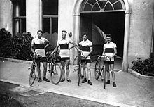 Photographie montrant les quatre cyclistes français debout à côté de leurs vélos devant l'entrée d'un bâtiment.