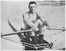 Fotografía que muestra a John Kelly sentado en su bote con un remo en cada mano.