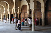 Fotografia de um grupo de turistas no pórtico da baía dupla, precedendo o salão de orações.  Esta é totalmente fechada, do lado do pórtico, por portas de madeira talhada.