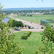 Una struttura in cemento e acciaio sostiene un'autostrada moderatamente trafficata che attraversa il fiume visto a sinistra.  Ci sono paludi e una città sullo sfondo.
