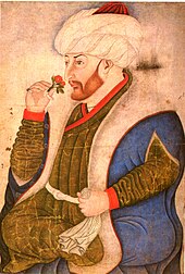 A corpulent bearded young man holding a rose and wearing a turban