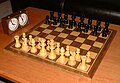 Šachové kameny v základním postavení na šachovnici společně s šachovými hodinami