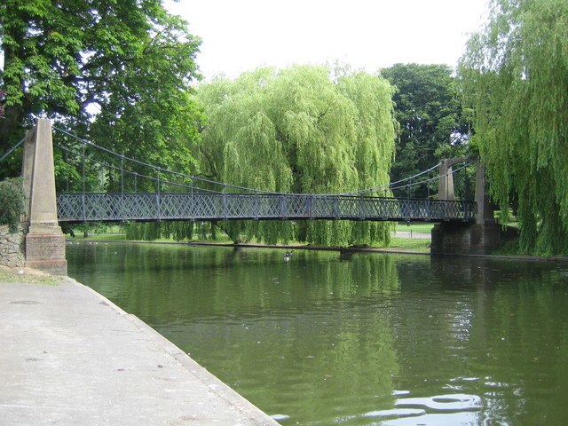 A pedestrian suspension bridge spans the boating lake created where the widened river flows through Wardown Park in Luton.