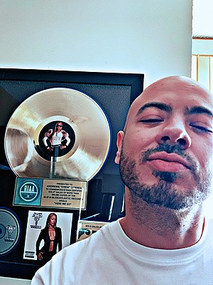 man smiling at camera with golden single certifiation award hanging on wall behind him