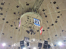 Photo de la bannière dédiée à Michel Briere au milieu de câbles tombant du plafond de la Mellon Arena; on distingue également les drapeaux américains, canadiens et la bannière dédiée à Mario Lemieux.